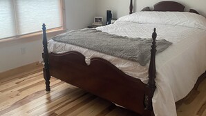 A bedroom with a wooden bed, a nightstand, a bedside table, a ceiling fan, and a window with blinds.