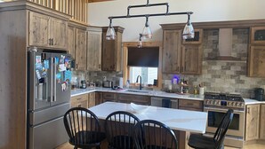 A kitchen with wooden cabinets, a stainless steel refrigerator, a large island with bar stools, and a gas stove.