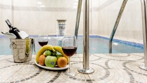 Una mesa junto a la piscina con un cuenco de fruta, una copa de vino y un balde de metal.