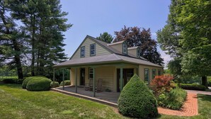A two-story house with a covered porch, surrounded by well-maintained lawns and trees. - Highville Hideaway - 2 bed, 1 bath, country views (Conestoga)