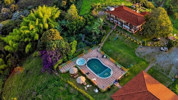 An aerial view of a property with a swimming pool, a house with a red roof, and surrounding lush greenery. - Finca Hotel La Moni (Circasia)