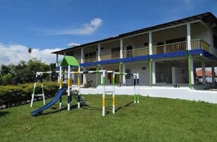Un parque infantil con tobogán y estructuras para escalar frente a un edificio con porche cubierto.