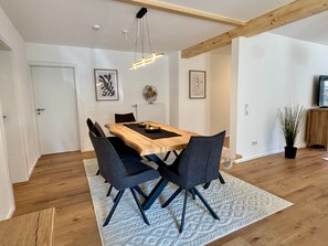 A dining area with a wooden table, four chairs, a patterned rug, and a ceiling light fixture.