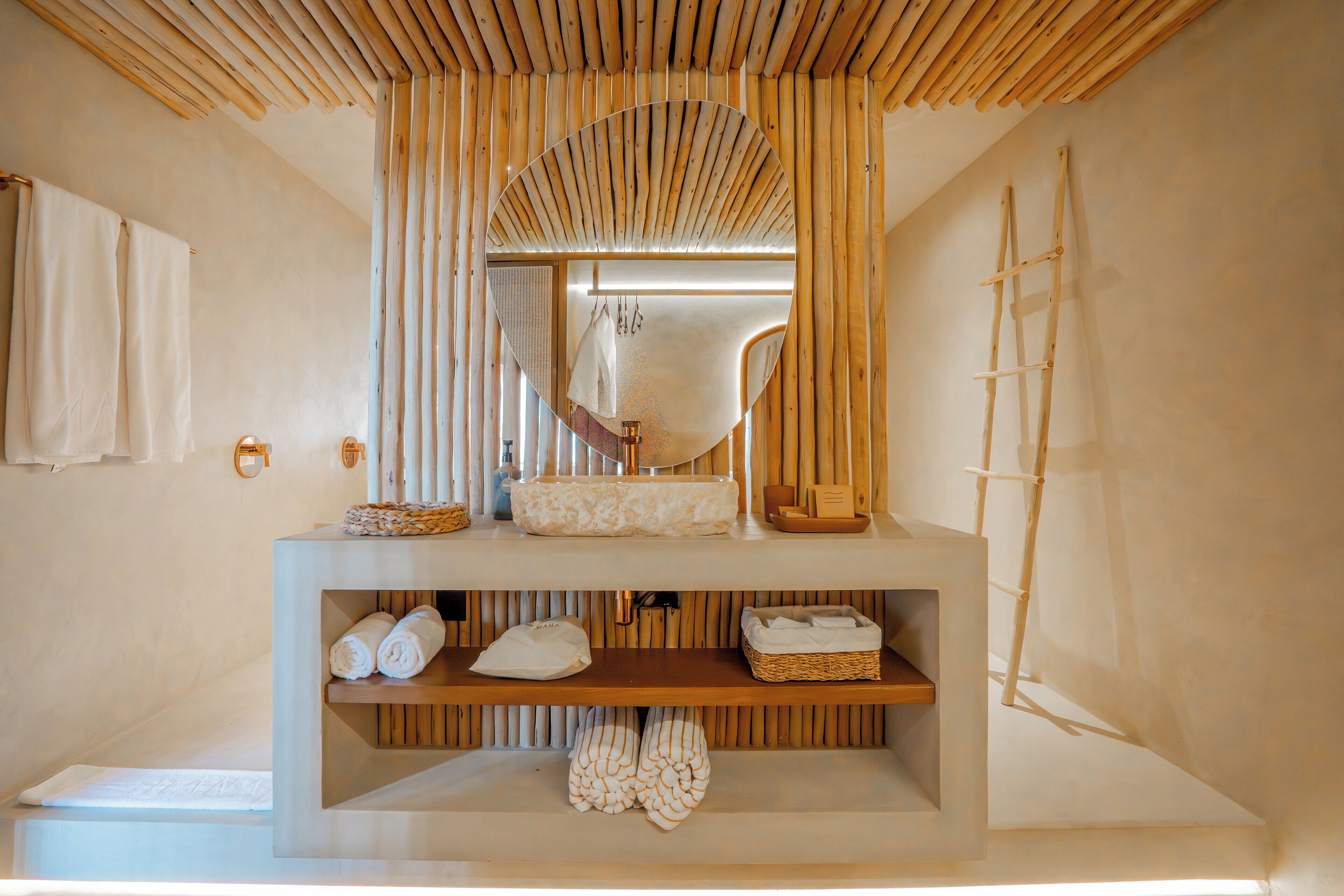 Un bagno con soffitto in listelli di legno, un grande specchio, una scala in legno e mensole con asciugamani e prodotti per l'igiene personale.