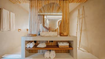 Un bagno con soffitto in listelli di legno, un grande specchio, una scala in legno e mensole con asciugamani e prodotti per l'igiene personale.