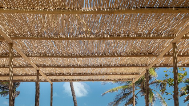 Un salon de plage doté de mobilier en bois, d’un toit de chaume et offrant une vue sur l’océan.
