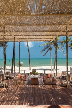 A beachside lounge with wooden furniture, a thatched roof, and a view of the ocean. - Mana Cumbuco Hotel (Caucaia)