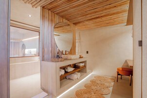 Un moderno cuarto de spa con techo de madera, un espejo grande, repisas con toallas y un tapete tejido en el suelo.