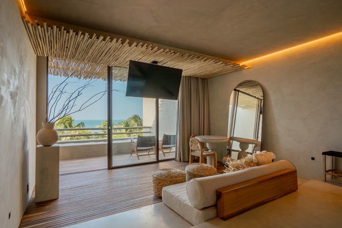 Une chambre moderne dotée d’une grande télévision, d’un canapé, d’une table à manger et d’un balcon offrant une vue sur l’océan.