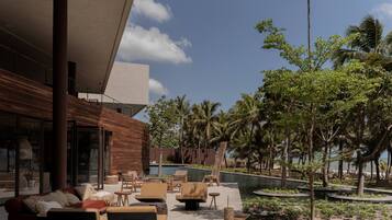 Uma área de estar ao ar livre moderna, com assentos e piscina, rodeada por palmeiras e vegetação.