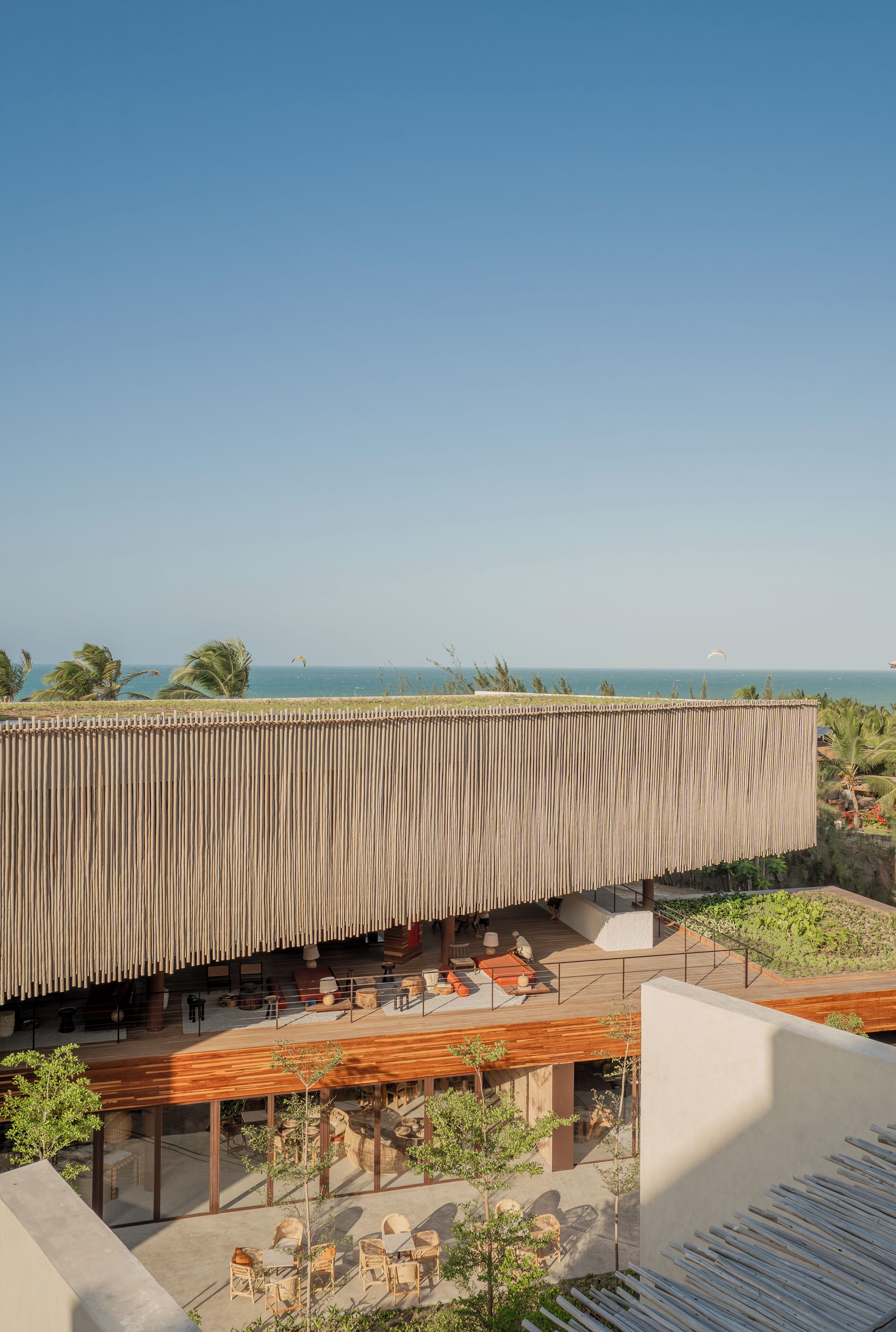 Um edifício moderno com deck de madeira e área de estar externa, com vista para uma praia e oceano.