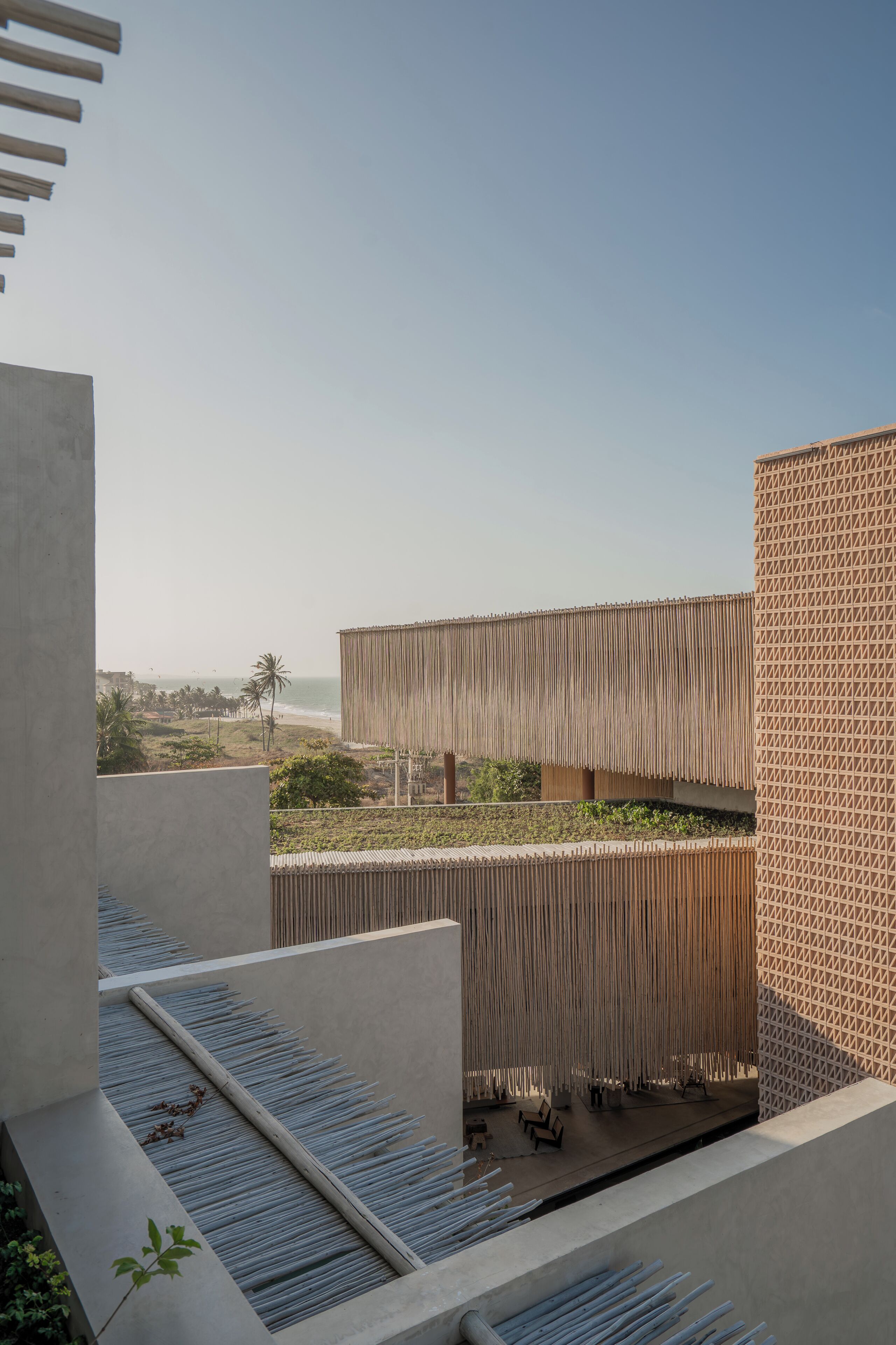 Un edificio moderno con una fachada singular, una terraza en la azotea con mobiliario y vistas a la playa.