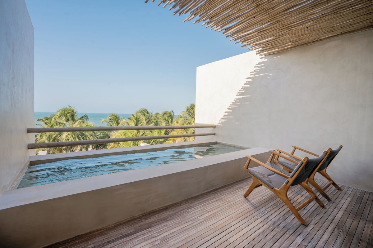 A balcony with a pool, wooden deck, and chairs.
