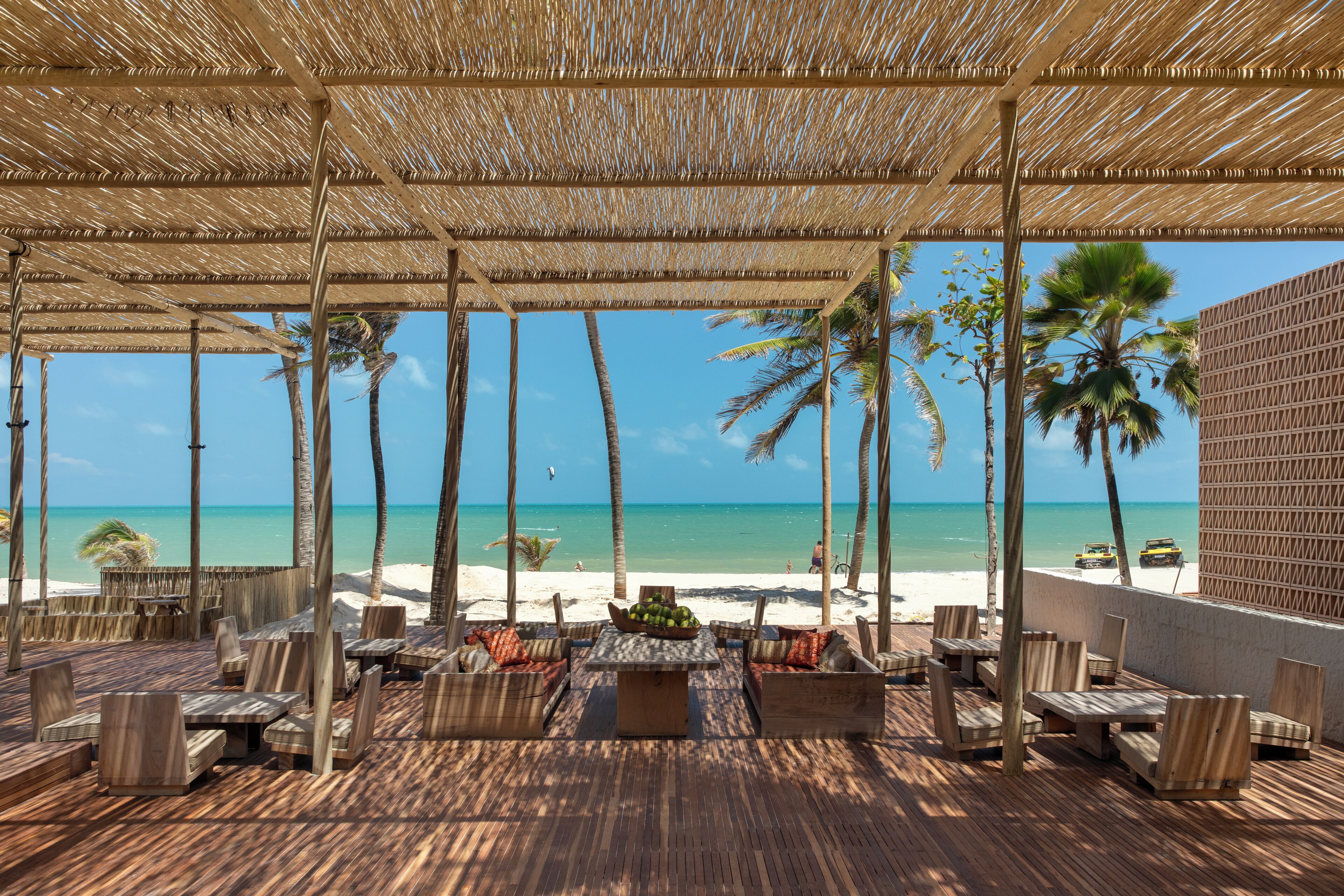 Un patio frente a la playa con muebles de madera y techo de paja, con vista al océano.
