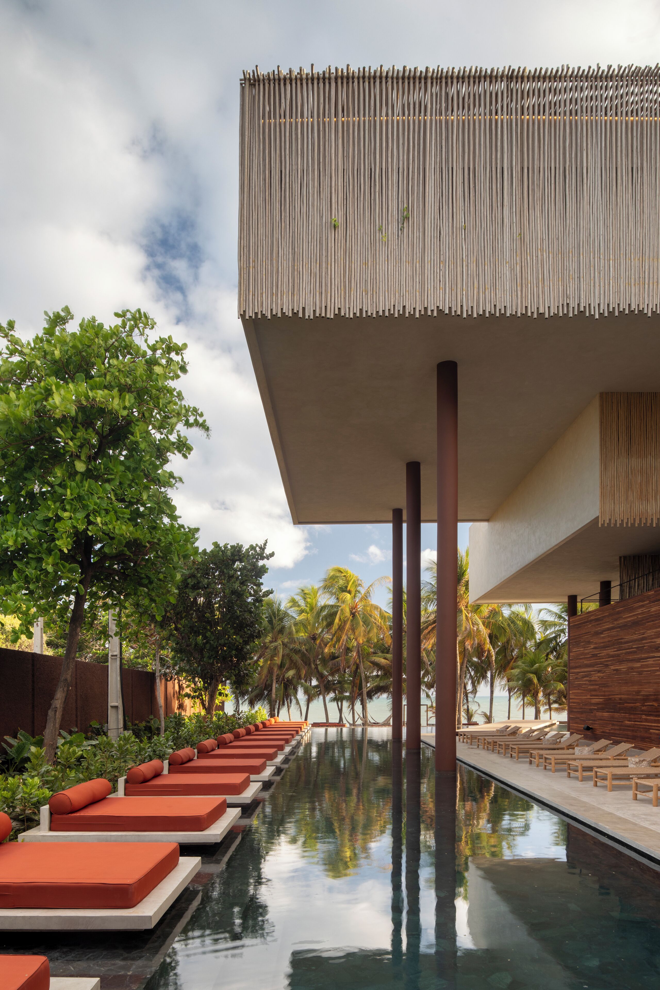 A poolside area with lounge chairs, a clear pool, and a modern building with vertical wooden slats.