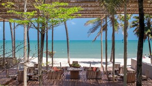 Un salon de plage doté de mobilier en bois et d’un toit de chaume, offrant une vue sur l’océan.