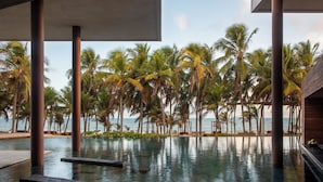 Une piscine à débordement bordée de palmiers, offrant une vue sur l’océan.