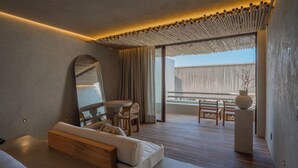 Une chambre d’hôtel moderne avec un grand lit, un coin salon avec une table et des chaises, un grand miroir et une vue sur l’extérieur.