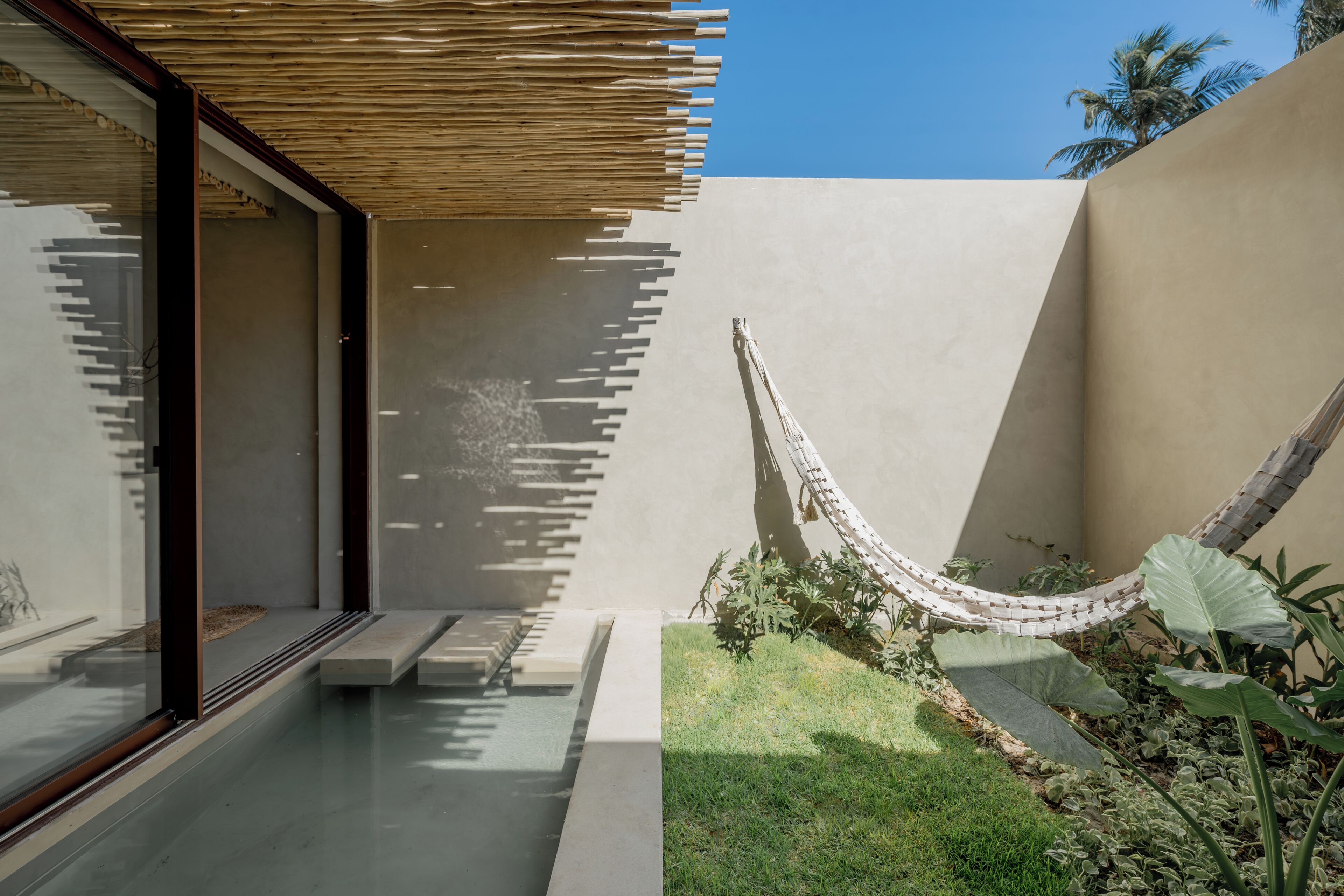 Un espacio exterior moderno con una hamaca, un banco de hormigón y un pequeño jardín.