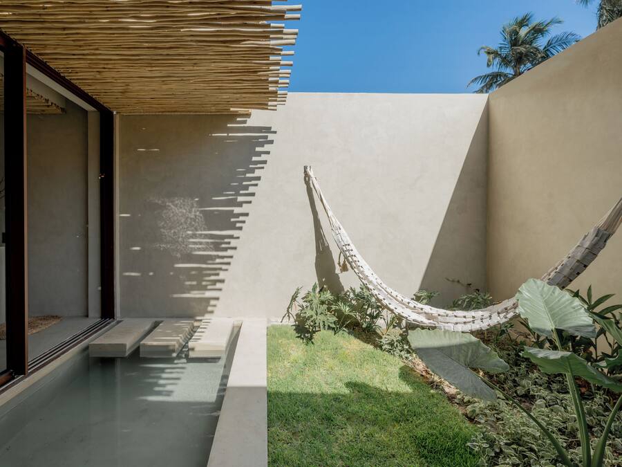 Un espacio exterior moderno con una hamaca, un banco de hormigón y un pequeño jardín.