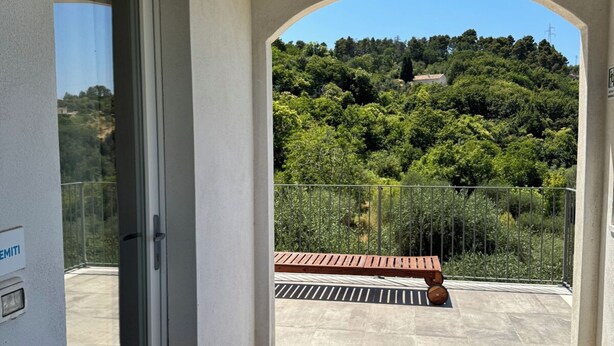 A balcony with a view of a forested hillside, a wooden bench, and a glass door. - Tremiti (Vico del Gargano)