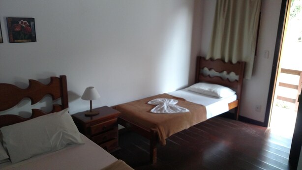 Une chambre d’hôtel avec un lit en bois, une table de chevet avec une lampe, une petite commode en bois et une fenêtre avec des rideaux.