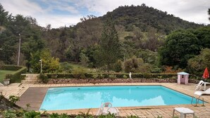 Une piscine rectangulaire bordée de pierres, entourée d’une terrasse dallée.