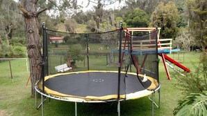 Un trampoline installé dans un espace herbeux, avec une balançoire et un arbre à proximité.