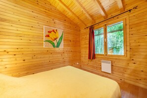A wooden cabin room with a bed, a window with curtains, and a wall-mounted air vent. - Holiday Home 'Chalet Sardane' with Mountain View, Shared Pool and Shared Terrace (Le Soler)