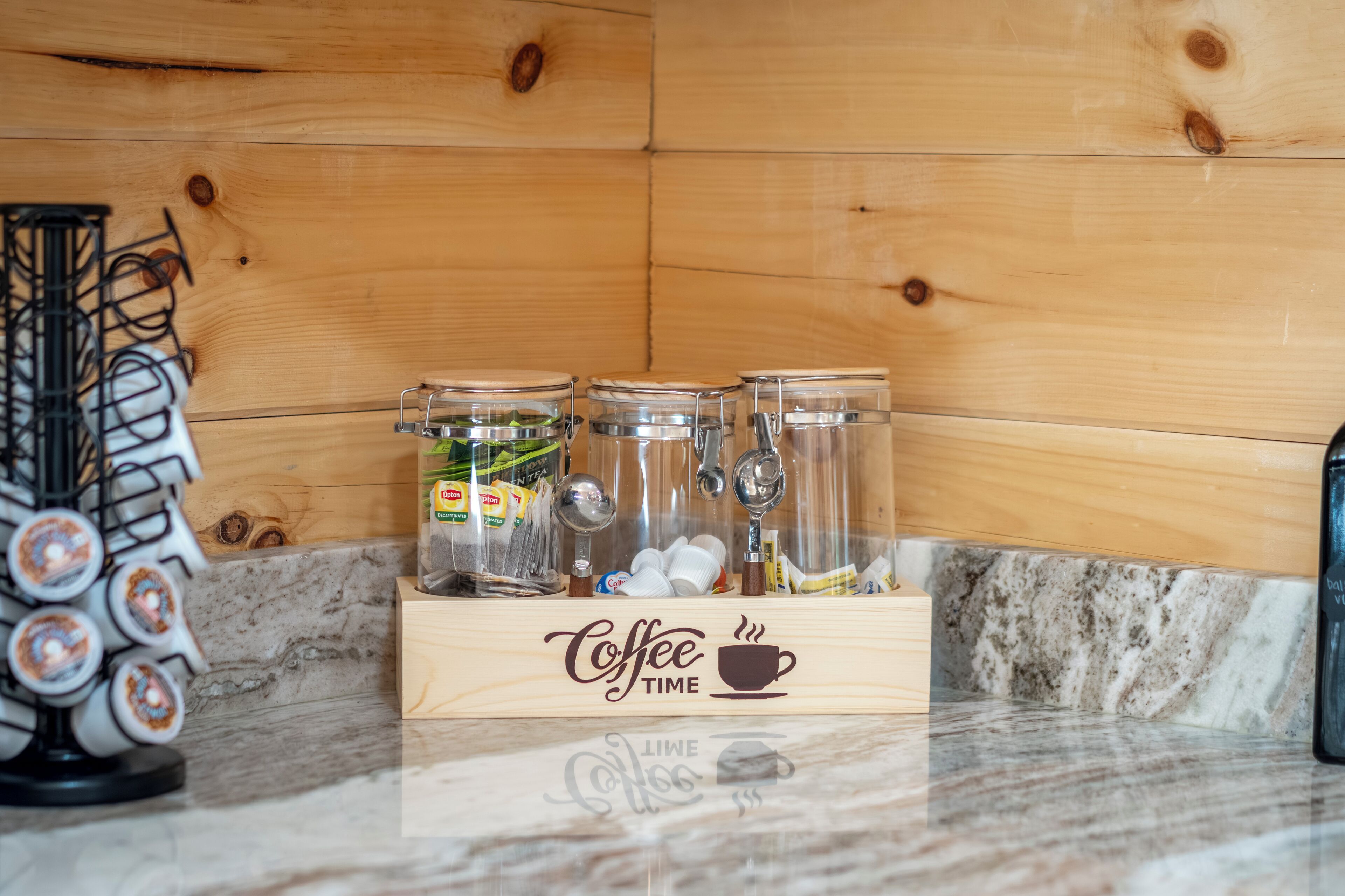 Une boîte en bois étiquetée « Pause café », contenant trois pots en verre remplis de café et de sucre, est posée sur un comptoir de cuisine.