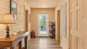 Un pasillo de madera con un escritorio de madera, una lámpara, una puerta que da al exterior y un estante con bolsas.