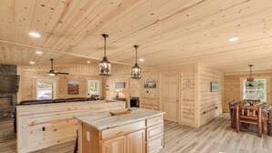 Una cocina amplia con armarios de madera, una isla central, iluminación colgante y un comedor con mesa y sillas de madera.