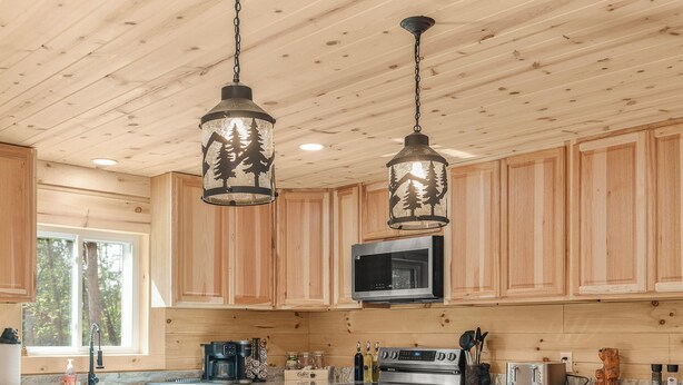 Una cocina con armarios de madera, una isla central con taburetes, electrodomésticos de acero inoxidable e iluminación colgante.