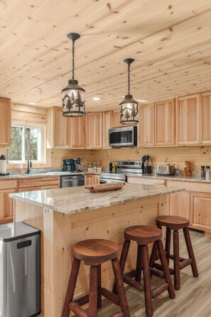 Une cuisine spacieuse avec des meubles en bois, un grand îlot central doté de tabourets, des appareils électroménagers en acier inoxydable et un éclairage suspendu.