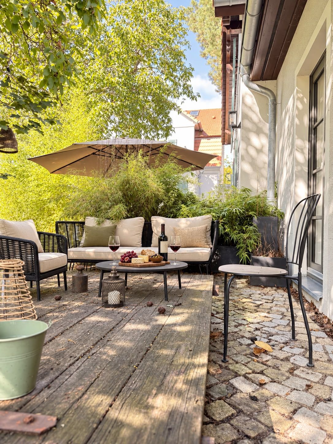 An outdoor seating area with a wooden deck, wicker furniture, and a table set with wine glasses, cheese, and grapes.