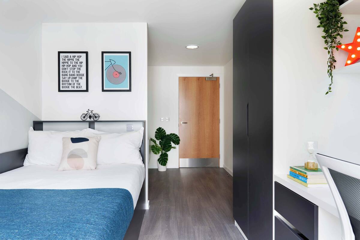 A modern bedroom with a bed, a desk, a plant, and a door.