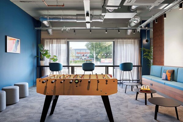 A modern room with a foosball table, two chairs, a sofa, and a window with a view of a building. - Westfield (Edinburgh)