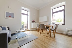 Una sala de estar moderna con sofá, mesa de centro, mesa de comedor con sillas y ventanas amplias.