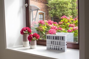 Un alféizar con un jarrón de flores y una caja de luz con el texto 'MOINMOIN HELLE STUUV'.