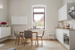 Una cocina moderna con comedor, suelo de madera, muebles blancos y una ventana con vistas.