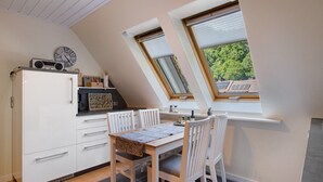 Une cuisine avec une table à manger, des meubles blancs, une horloge et une fenêtre avec des stores.
