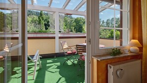 Une pièce donnant sur un jardin grâce à de grandes fenêtres, avec un radiateur et une table entourée de chaises.