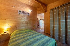 Een houten kamer met een bed, nachtkastje, lamp, koelkast en gordijn.