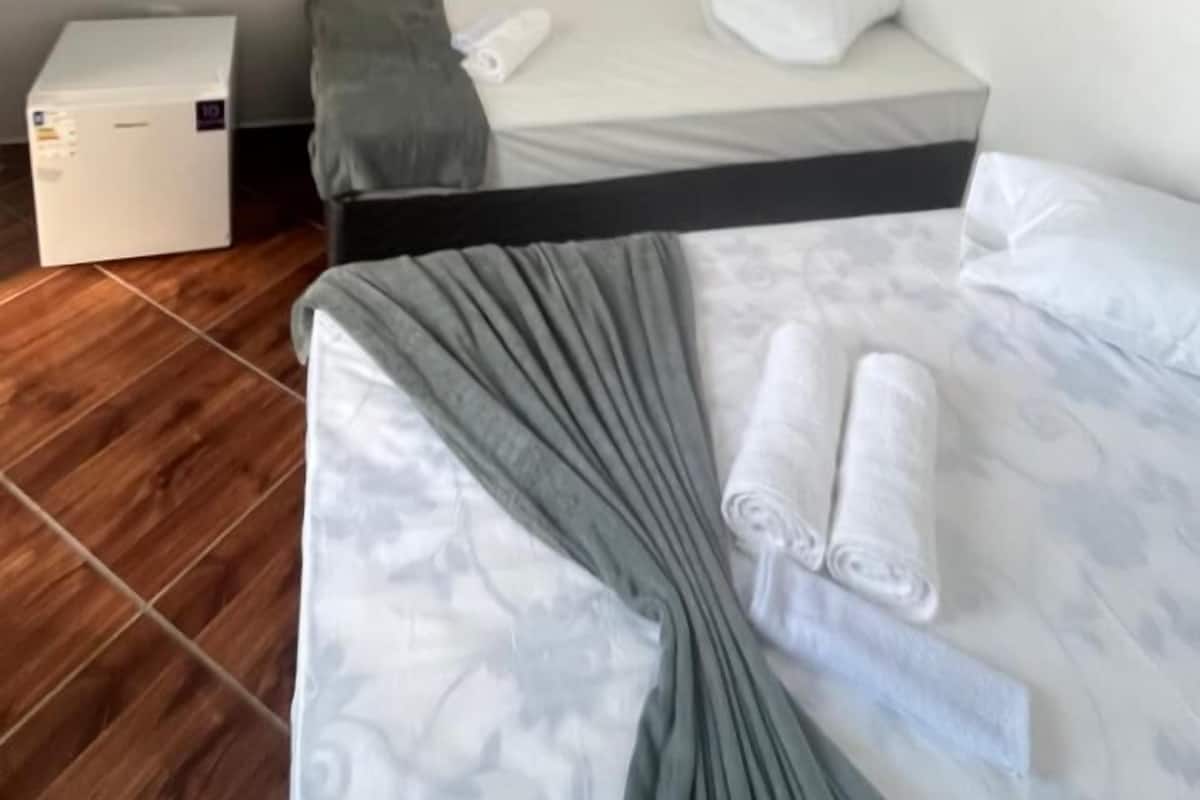 A hotel room with a bed, a small table, a TV mounted on the wall, and a refrigerator.