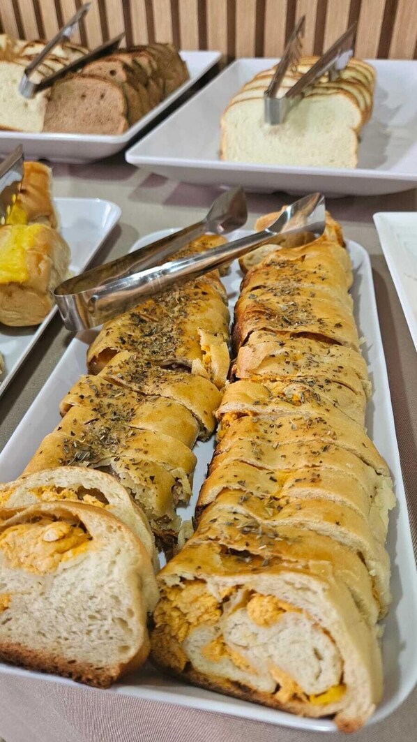 Ett buffébord med olika rätter, inklusive en stor limpa bröd med örter och ost, samt andra skivade brödsorter och bakverk.