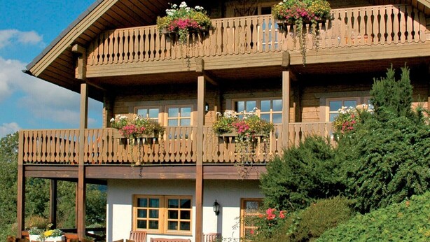 Een houten huis met twee verdiepingen, voorzien van balkons, houten leuningwerk en bloembakken.