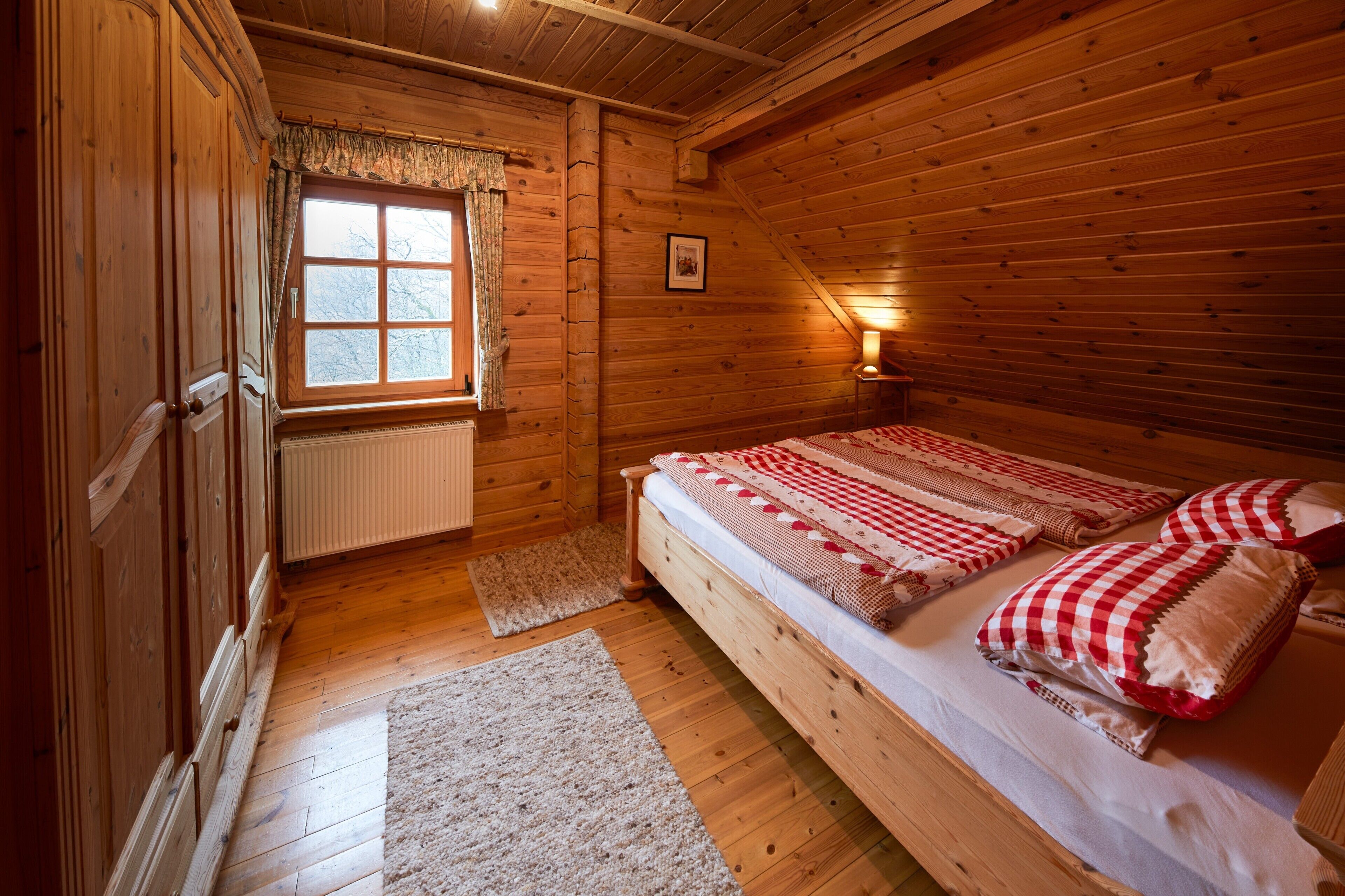 Une pièce dans un chalet en bois, comprenant un lit, une fenêtre, un radiateur et une lampe.