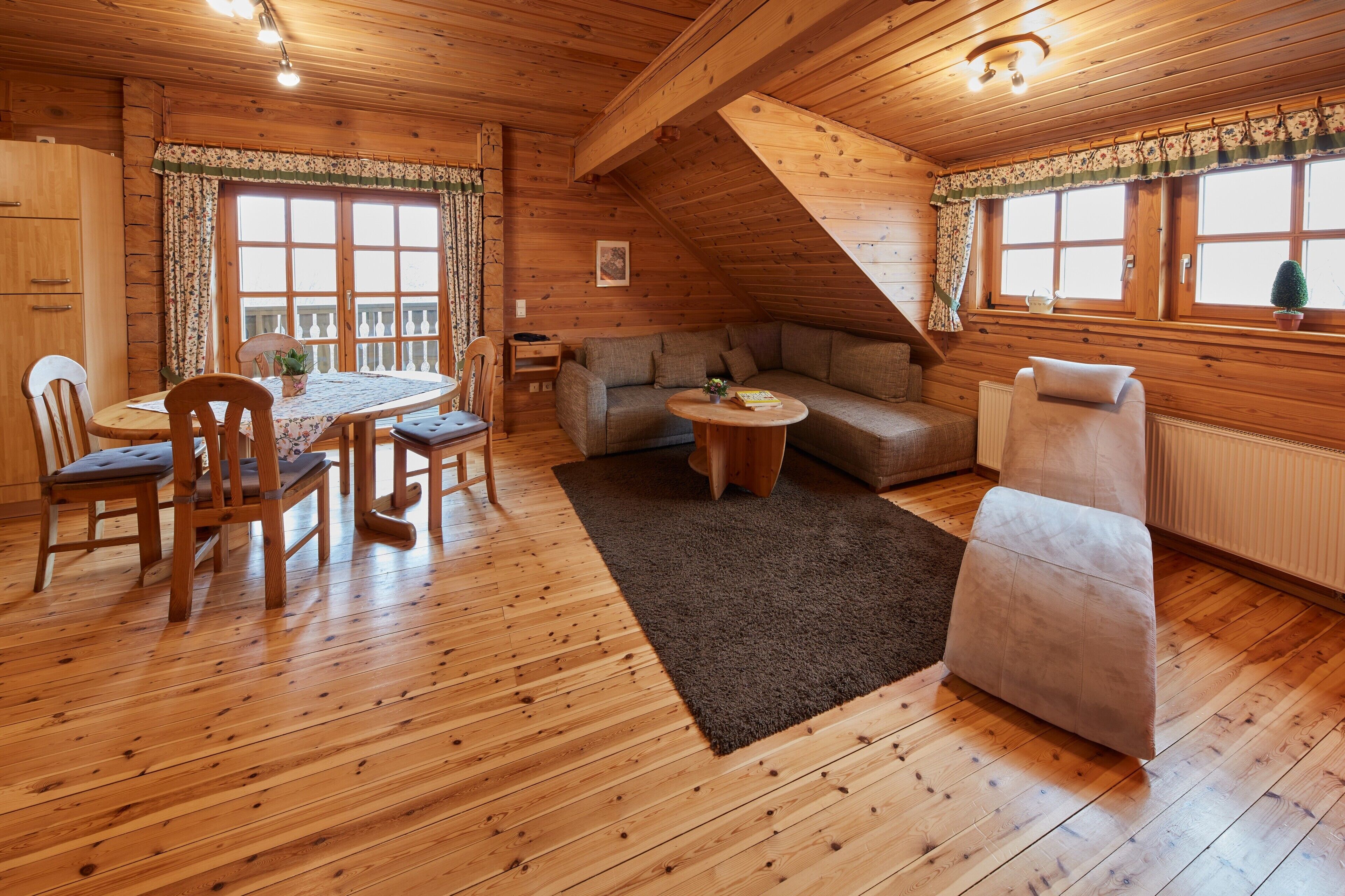 A wooden interior with a dining table, chairs, a sofa, and a small round table.