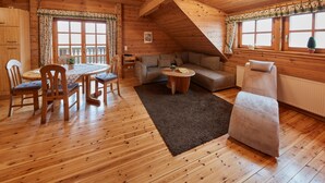 Een houten interieur met een eettafel, stoelen, een bank en een kleine ronde tafel.