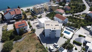 An aerial view of a coastal residential area with modern buildings, a swimming pool, and a road leading to the beach. - Apartment Nina - panoramic sea views (Slatine)